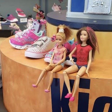 2 Dolls sitting in a Sketchers shoe store.