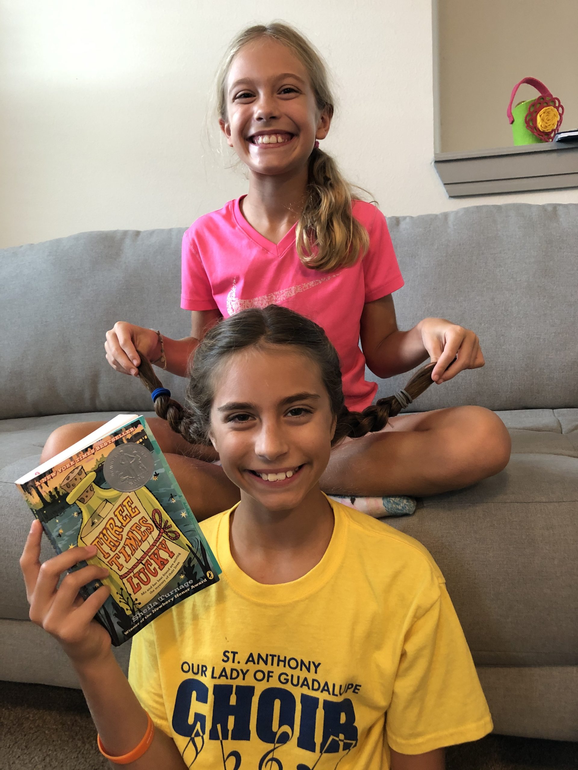 2 kids, girls, holding up the Three Times Lucky book, smiling at the camera.