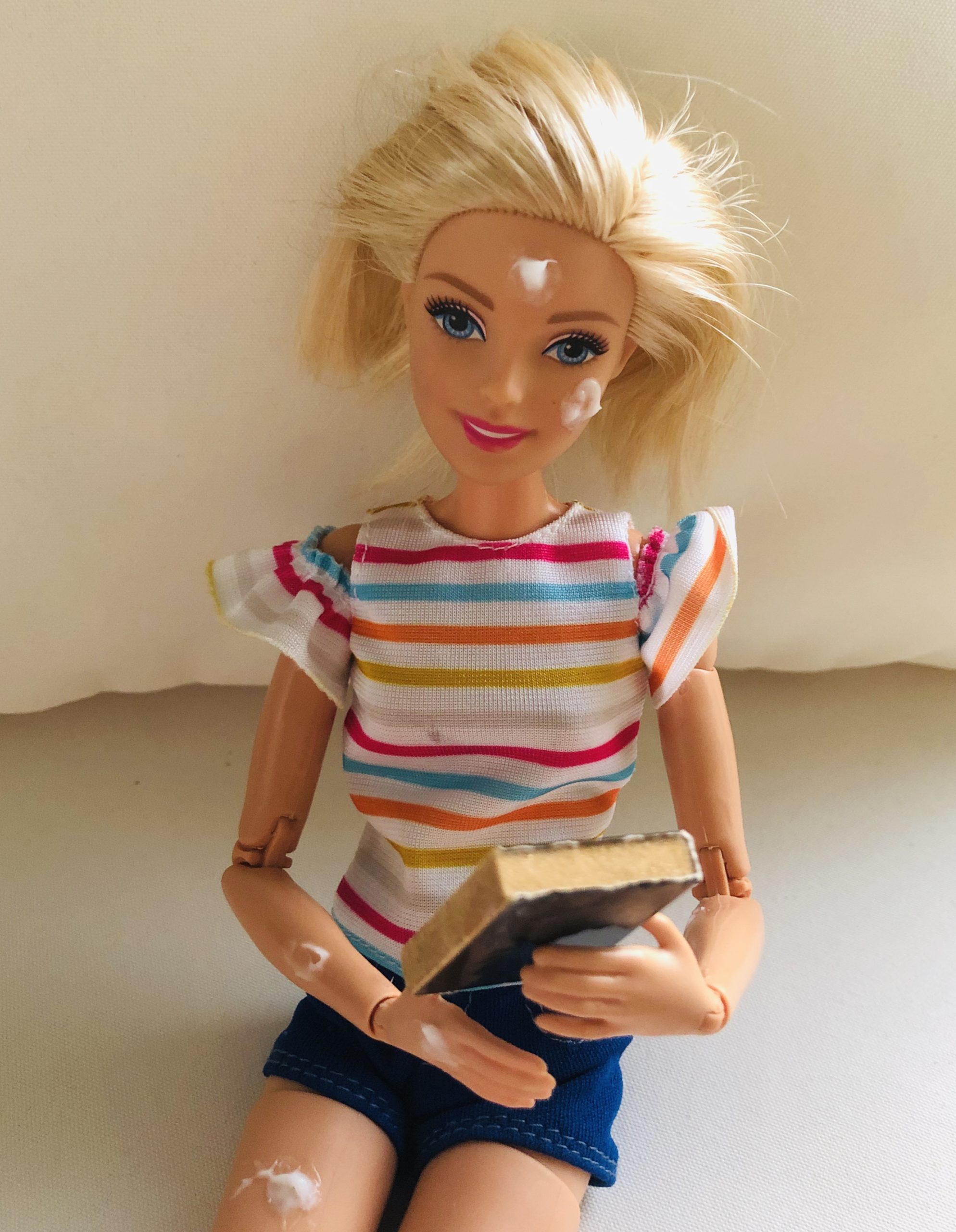 Barbie doll reading a book, wearing a rainbow colored striped shirt.
