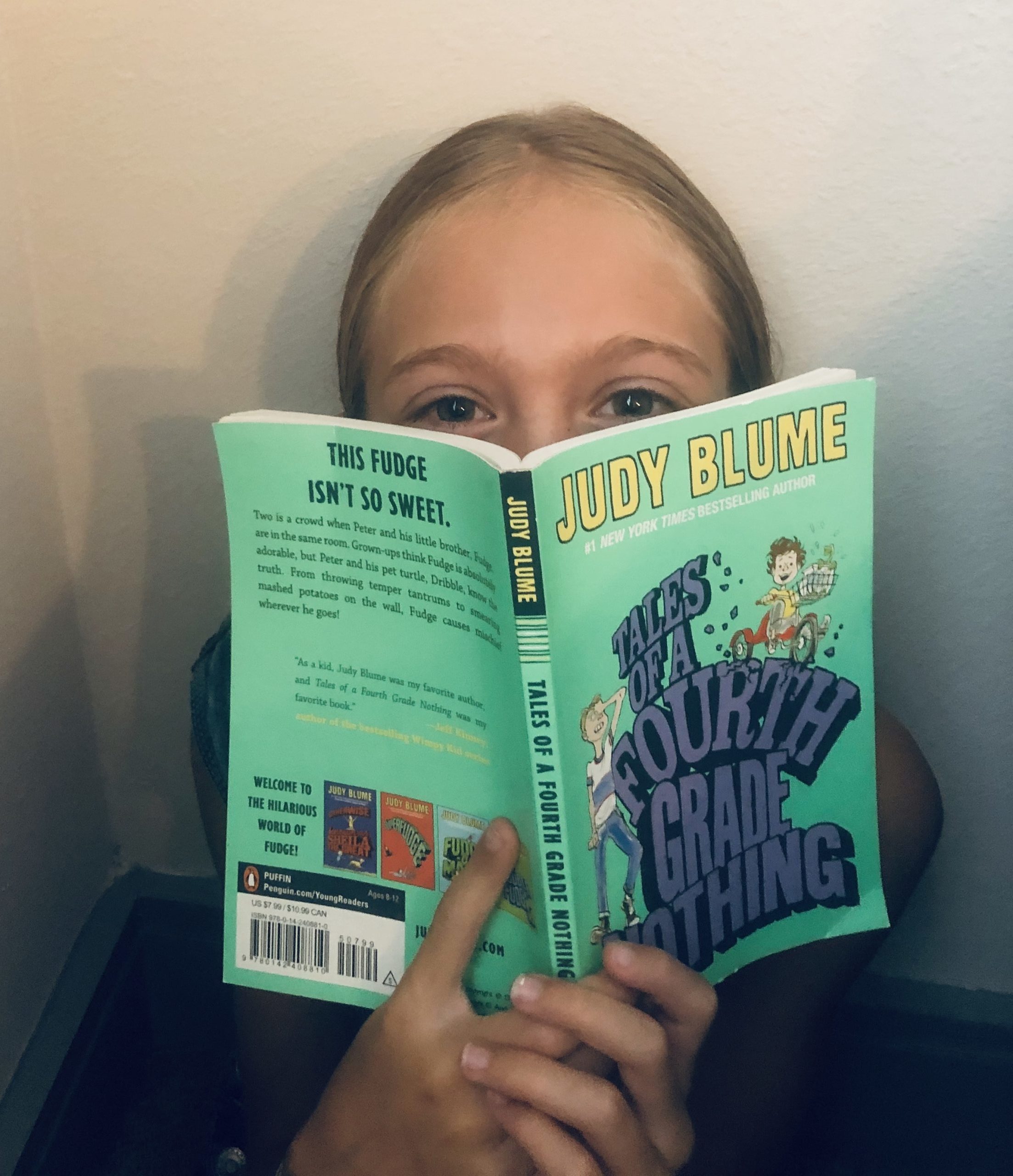 Brecken peeking over the book, Tales of a Fourth Grade Nothing by Judy Blume for the children's book review.