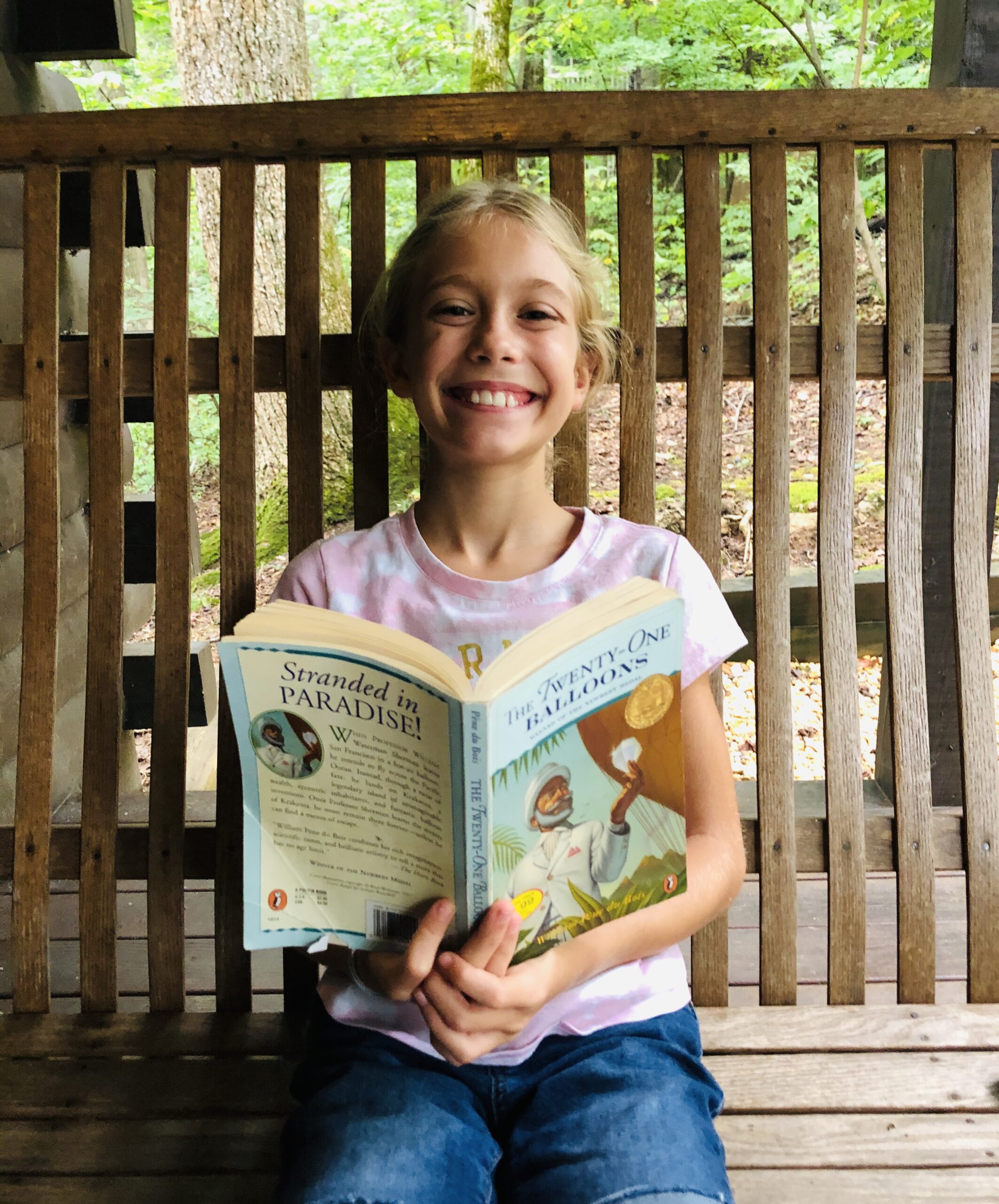 Blond haired Brecken sitting in a swing reading Twenty One Balloons for the Children's Book Review.