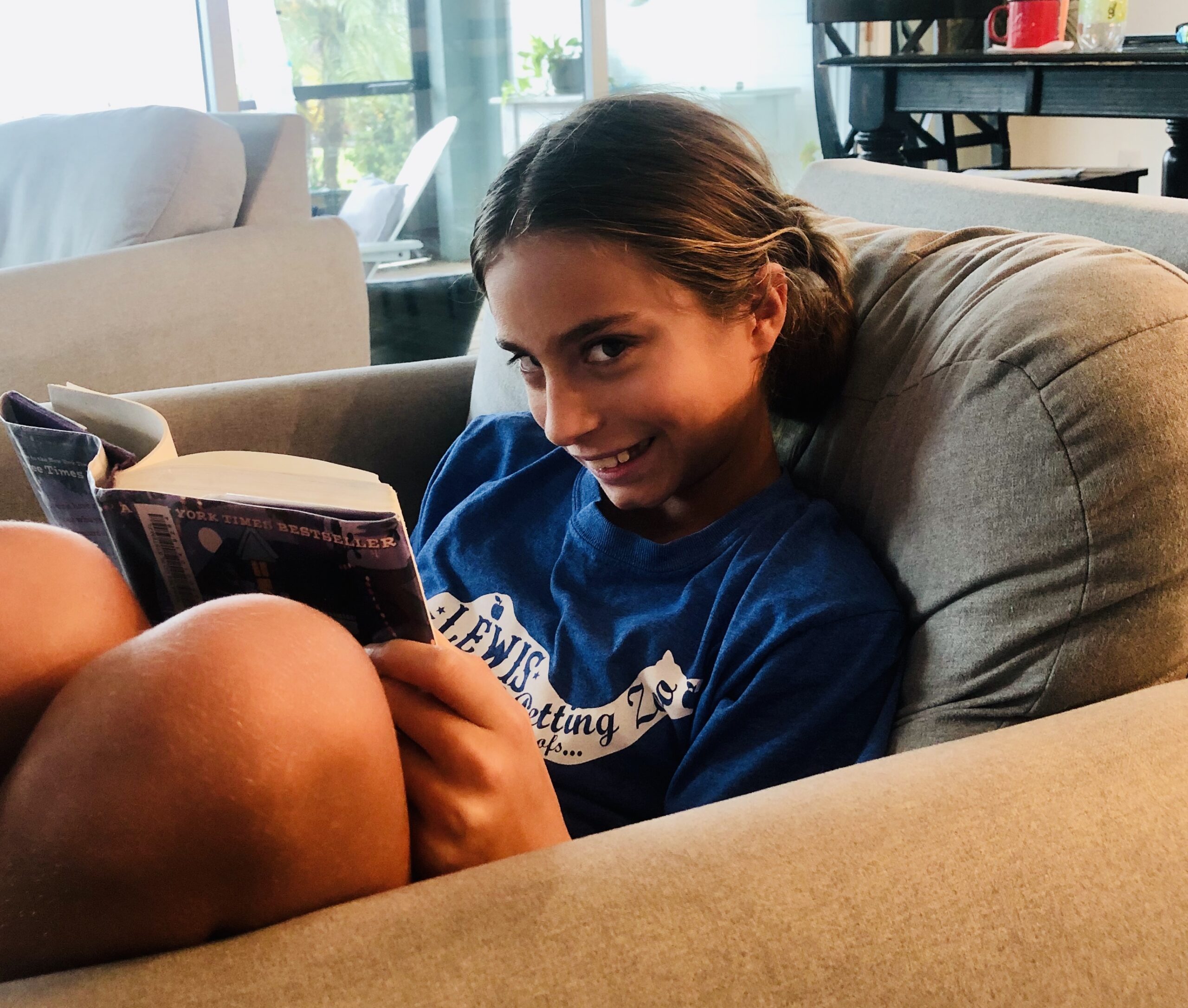 For the Children's book review on The Ghost of Tupelo Landing, a girl is reading the book, smiling at the camera. 