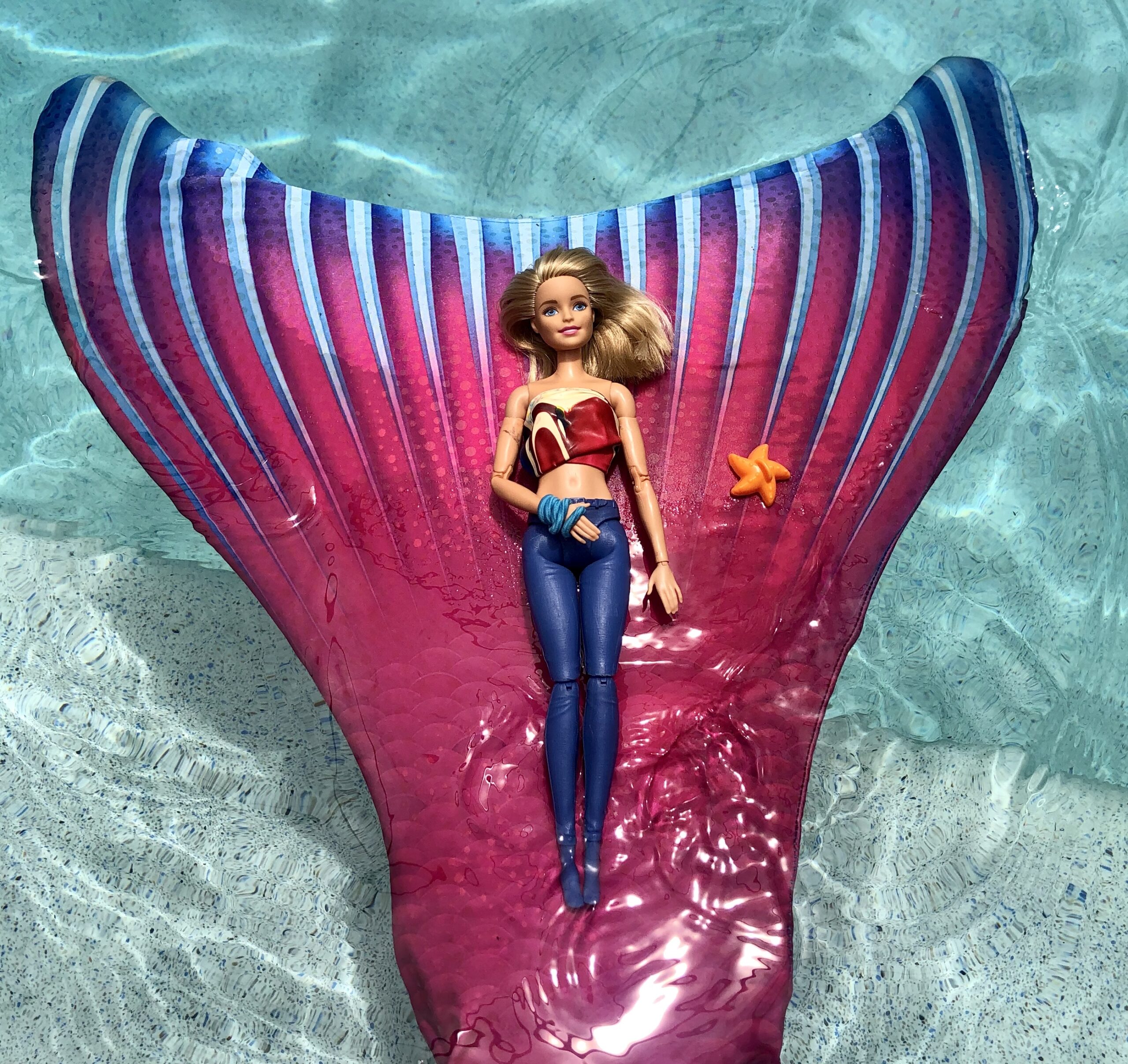 A Barbie Doll laying on a bright colored mermaid raft.
