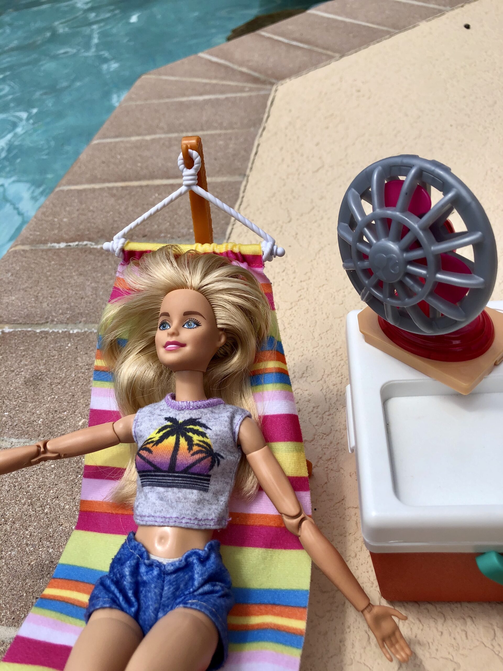 A barbie doll laying on a hammock by a pool.