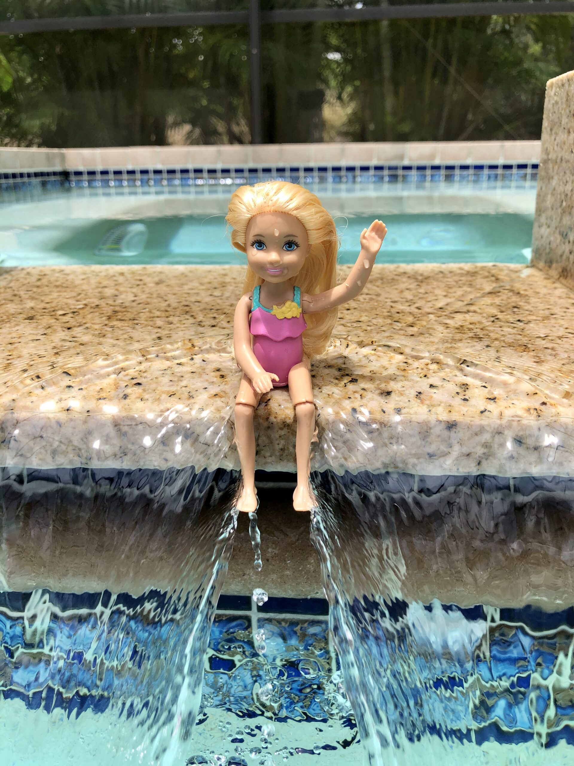 A Chelsea Doll, Rowan from the story Goodbye Costa Rica, sitting on a waterfall, waving her hand at the camera.