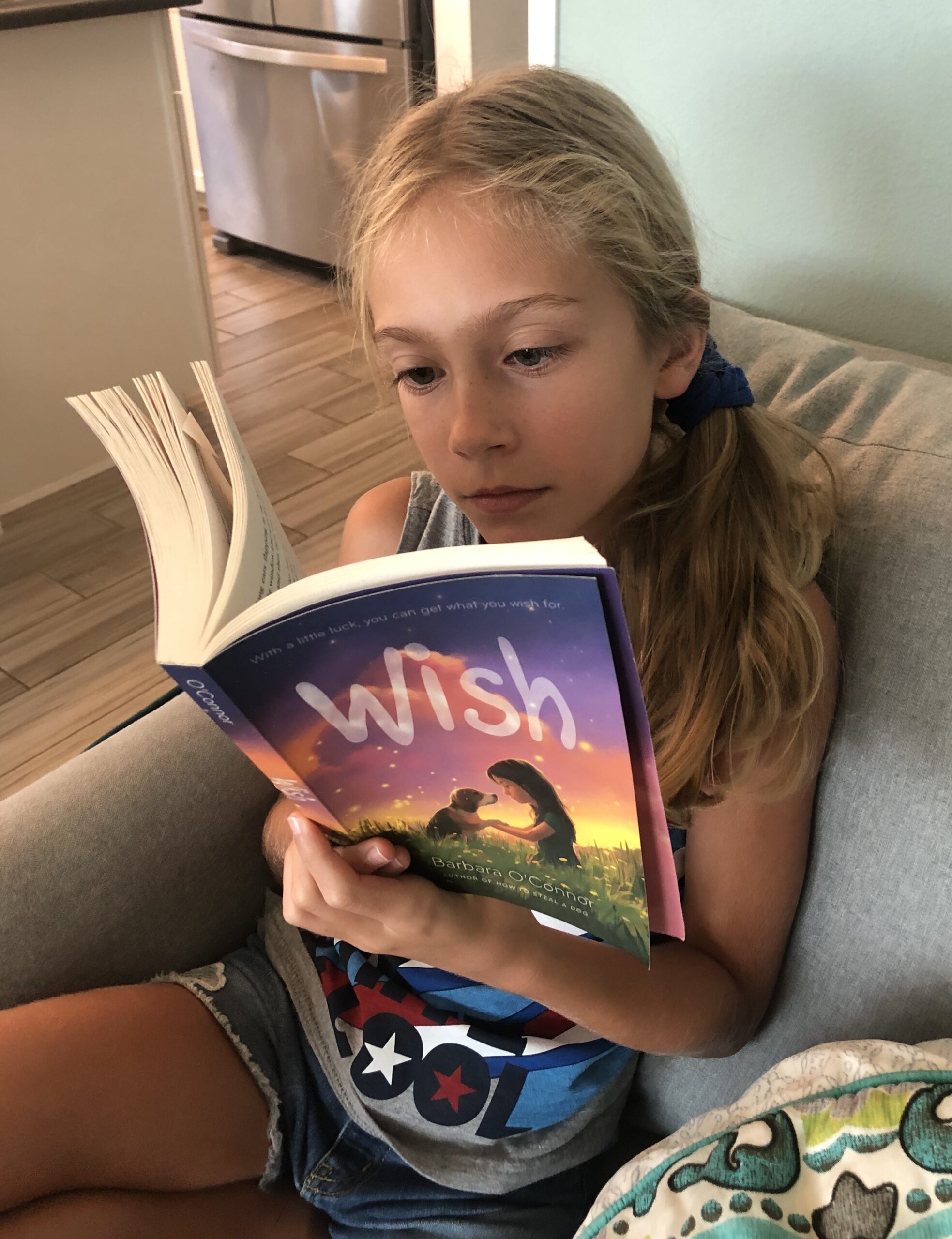 Blonde haired Brecken reading Wish by Barbara O'Connor for the children's book review.