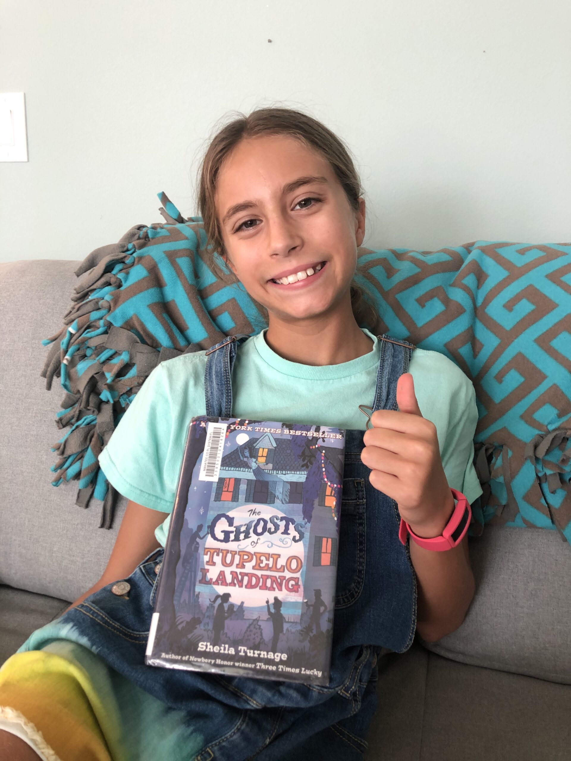 Kinley giving a things up while holding the book of The Ghosts of Tupelo Landing for the children's book review.