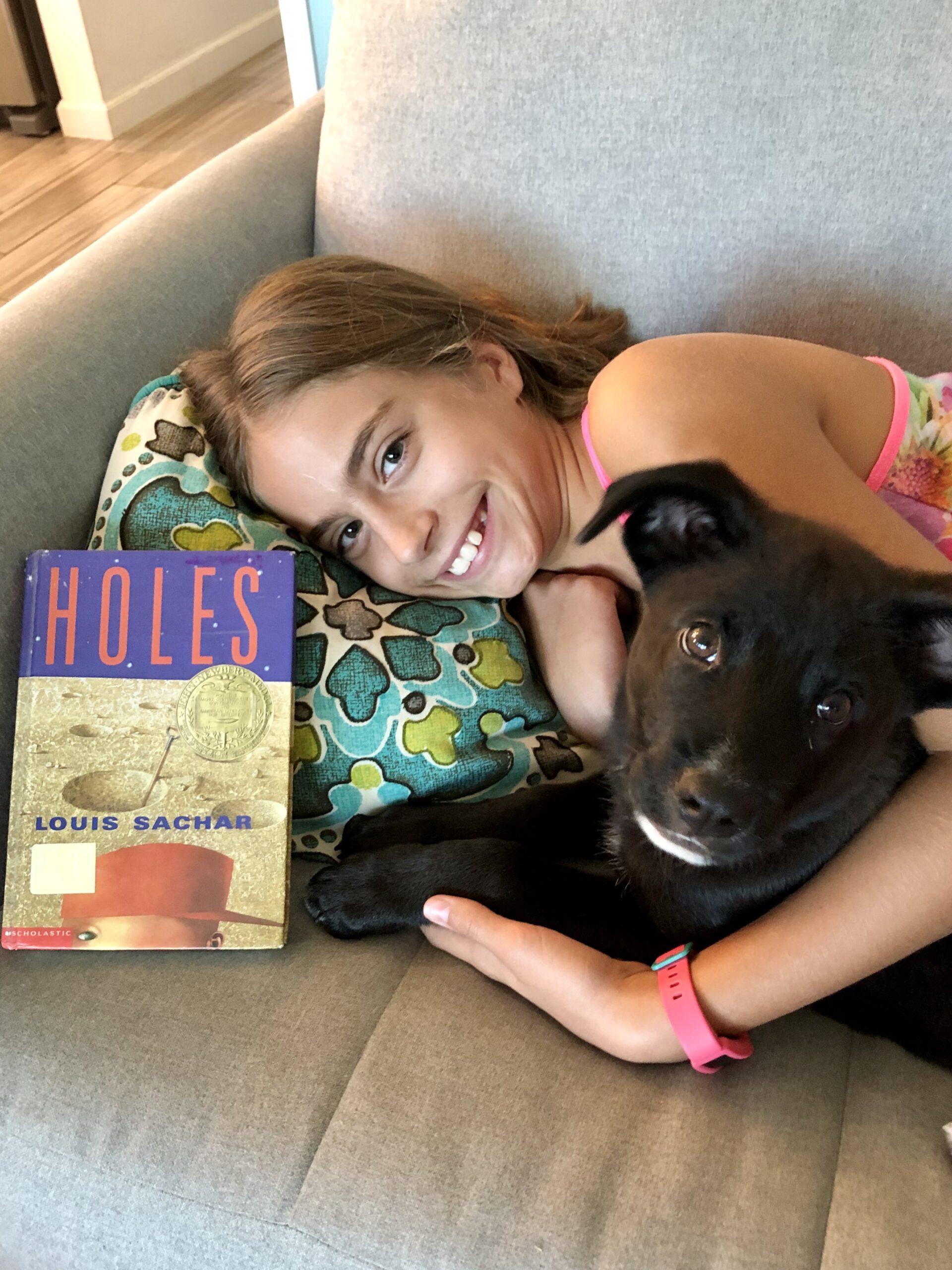 Girl laying down with her dog and the book Holes for this Book Review on it.
