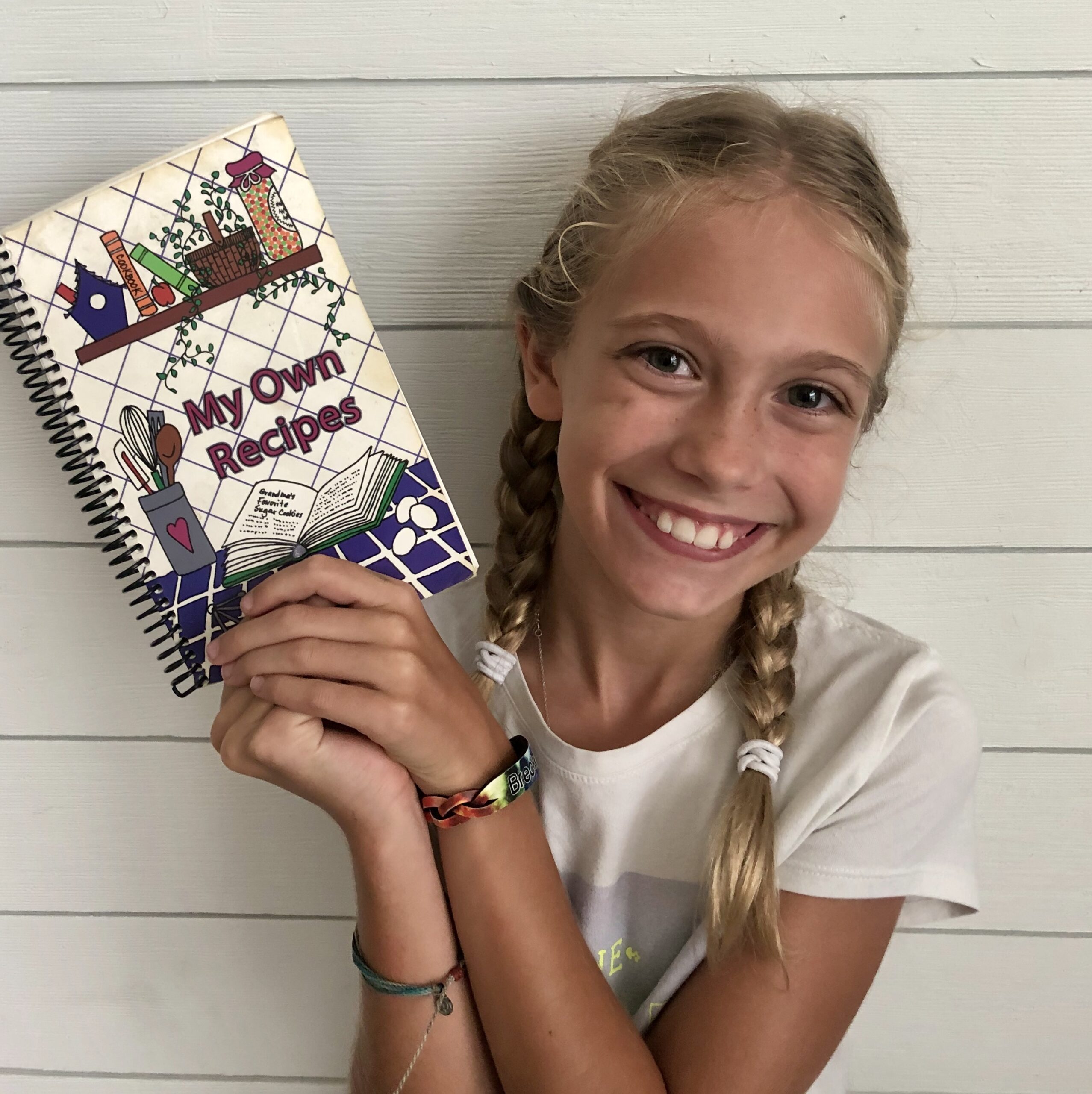 A blonde haired girl holding a recipe book.