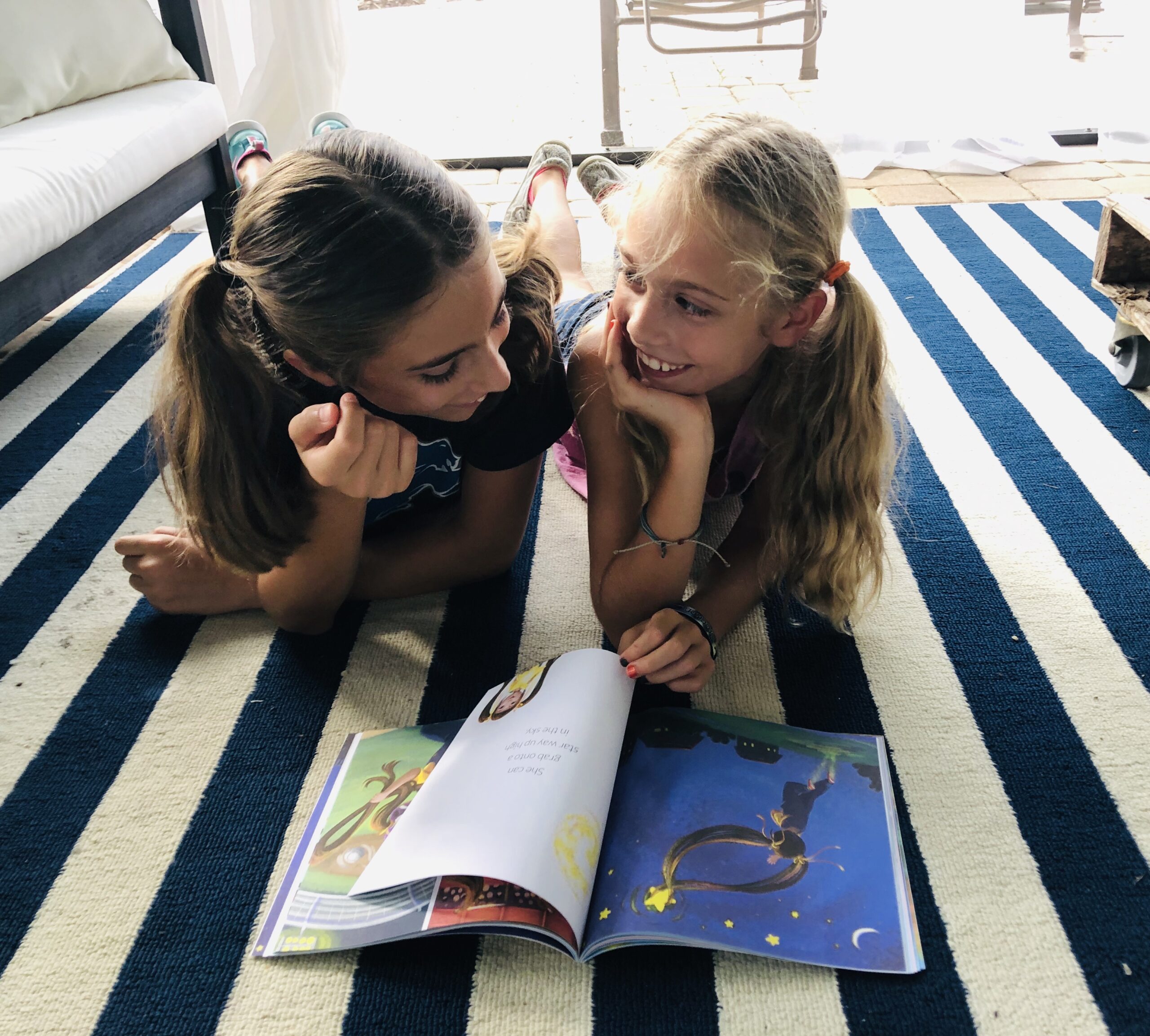 2 girls reading a book, smiling.