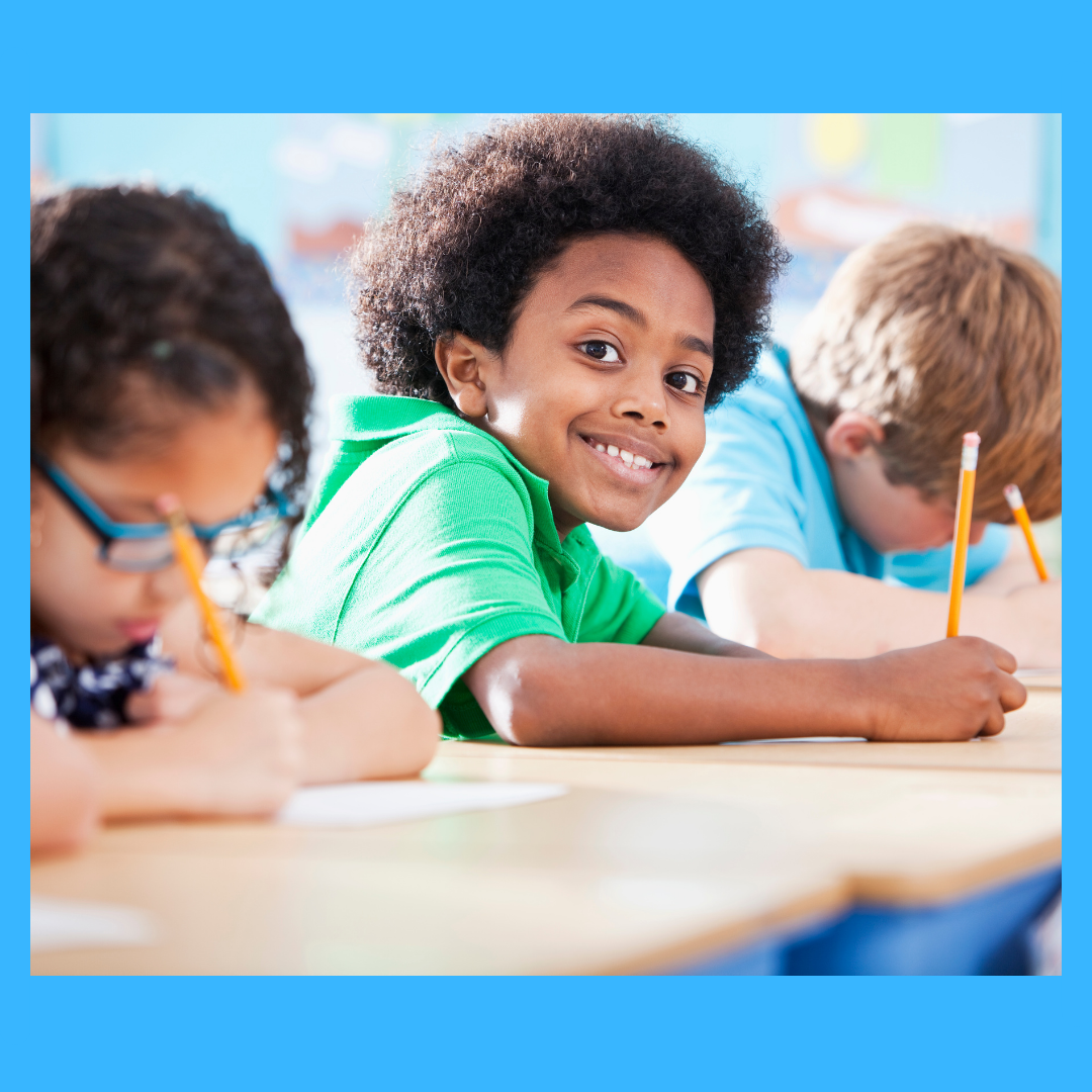 A kid in a classroom looking happy while writing.