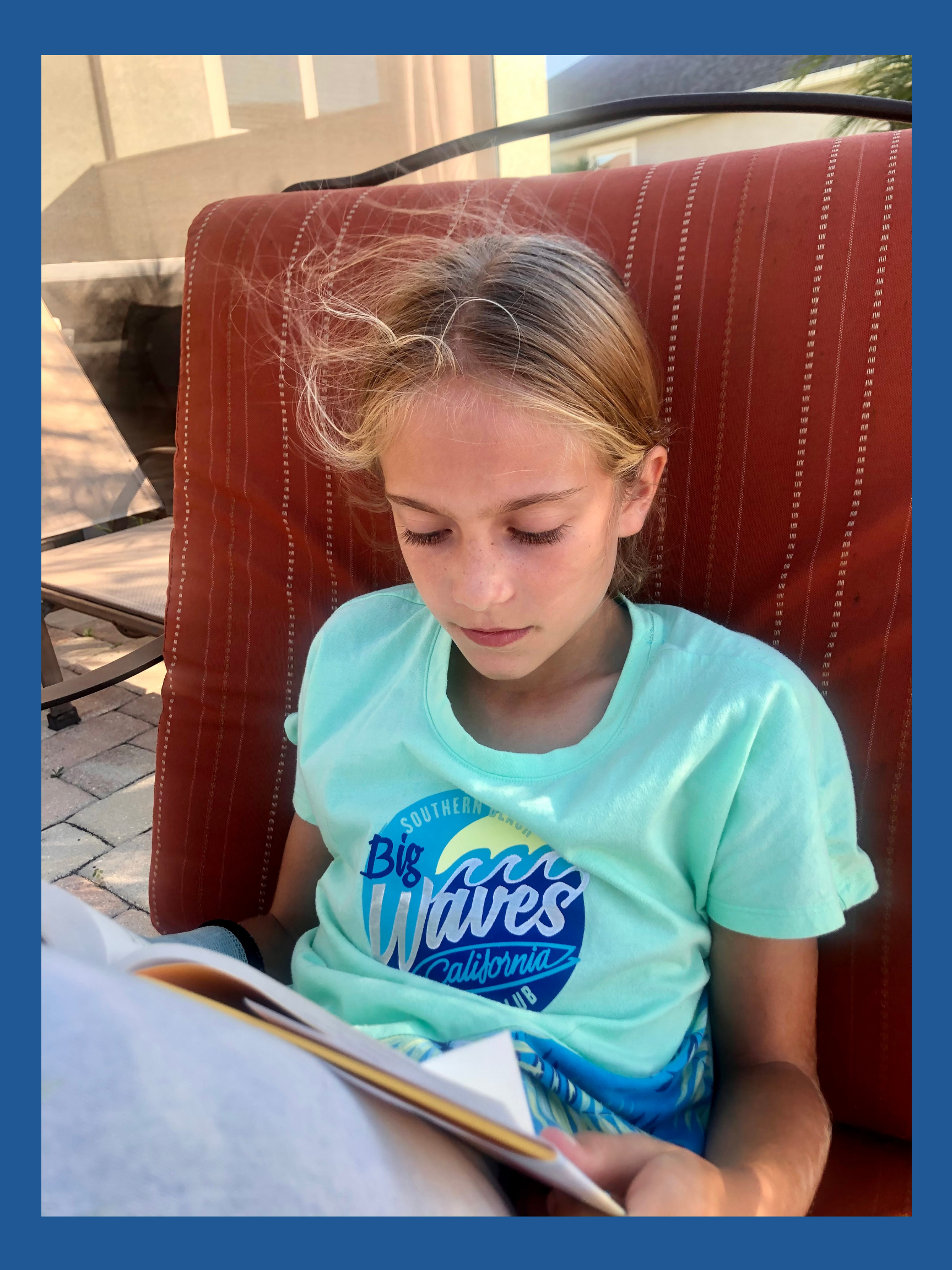 A blonde haired girl reading outside.