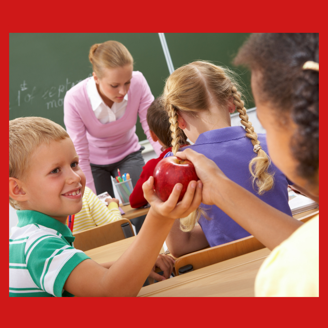 A boy being thoughtful, passing an apple to a friend.